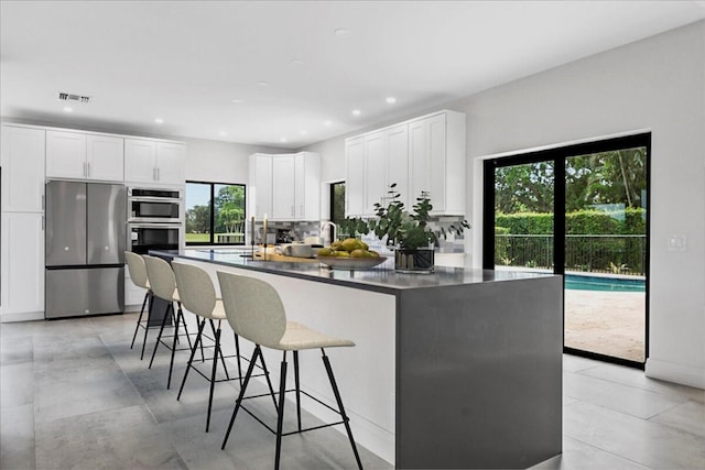 kitchen featuring white cabinetry, backsplash, stainless steel appliances, and a kitchen bar