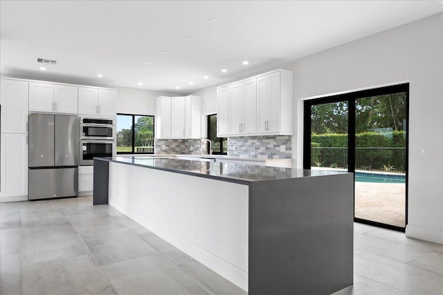 kitchen with sink, appliances with stainless steel finishes, white cabinets, a kitchen island, and decorative backsplash