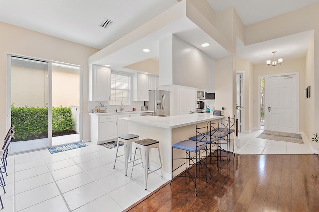 kitchen featuring white cabinetry, stainless steel fridge, a kitchen breakfast bar, light hardwood / wood-style floors, and kitchen peninsula