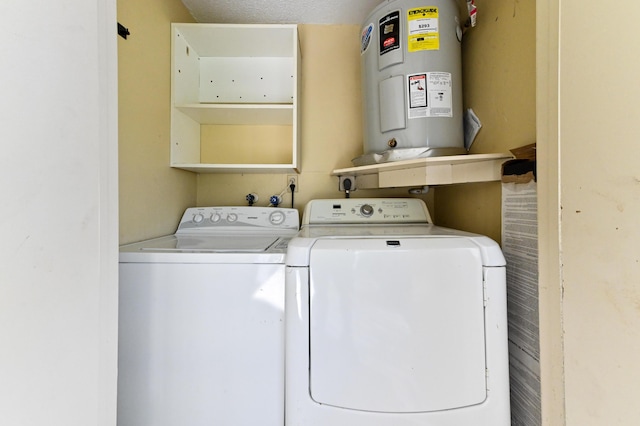 clothes washing area with laundry area, electric water heater, a textured ceiling, and washing machine and clothes dryer