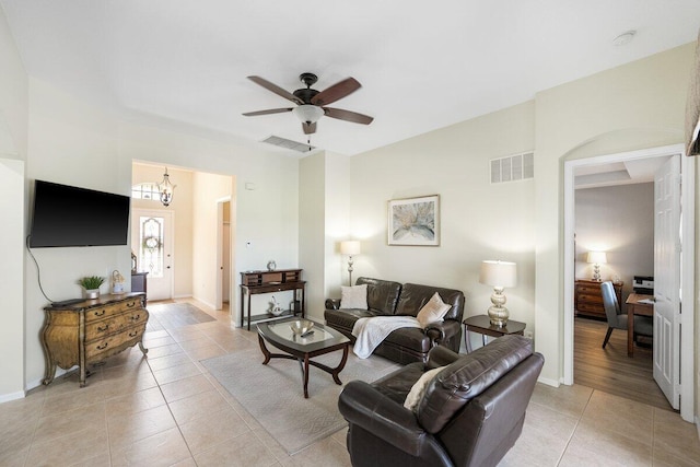 living room with light tile patterned flooring, visible vents, and ceiling fan with notable chandelier
