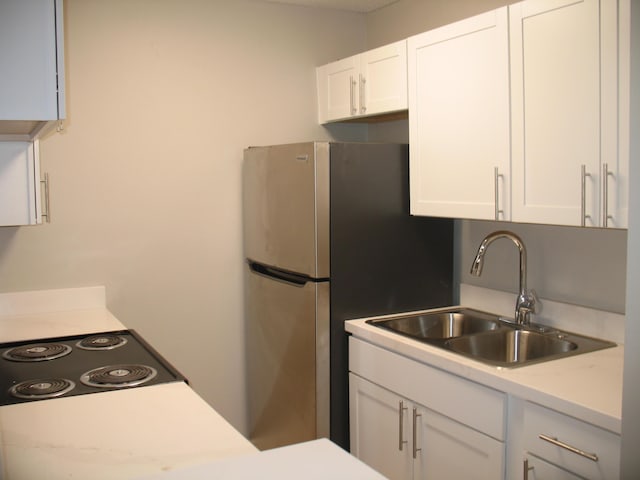 kitchen featuring light countertops, a sink, freestanding refrigerator, and white cabinets