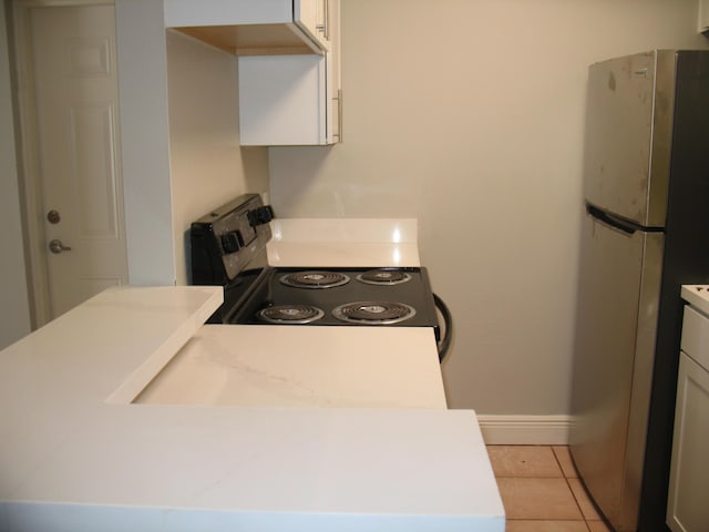 kitchen with electric range oven, freestanding refrigerator, white cabinets, light tile patterned flooring, and baseboards