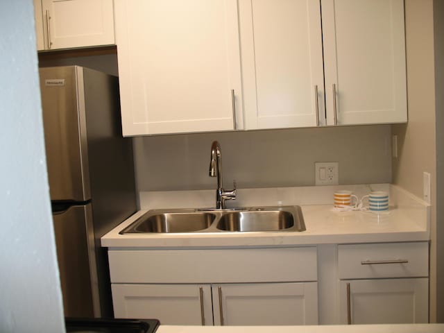 kitchen with freestanding refrigerator, white cabinets, a sink, and light stone countertops