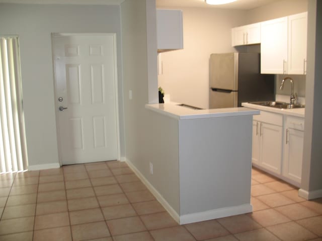 kitchen featuring light tile patterned floors, a sink, white cabinets, light countertops, and freestanding refrigerator