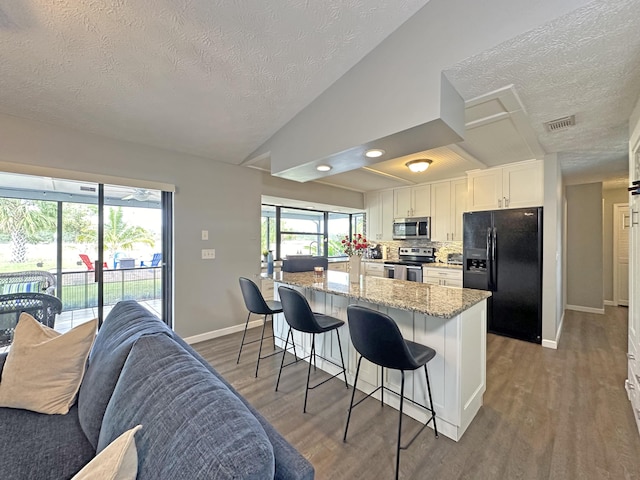 kitchen with lofted ceiling, appliances with stainless steel finishes, white cabinetry, light stone counters, and a kitchen bar