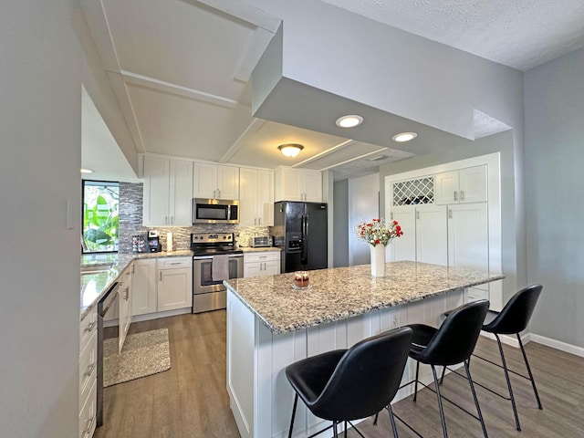 kitchen featuring appliances with stainless steel finishes, a breakfast bar, tasteful backsplash, white cabinets, and hardwood / wood-style flooring