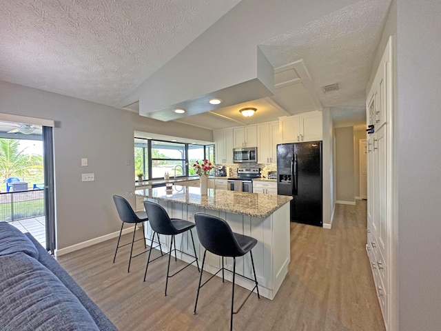 kitchen with stainless steel appliances, light stone countertops, white cabinets, a kitchen bar, and light wood-type flooring