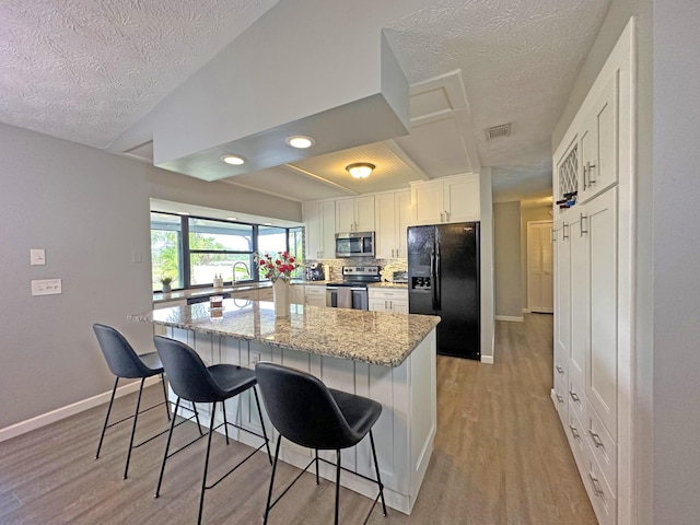 kitchen with appliances with stainless steel finishes, white cabinets, a kitchen bar, backsplash, and light stone counters