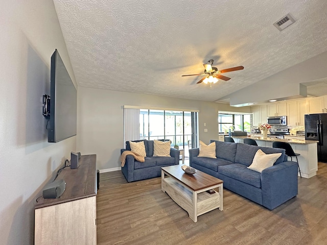 living room featuring lofted ceiling, hardwood / wood-style flooring, a textured ceiling, and ceiling fan