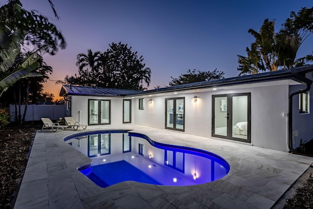 pool at dusk featuring french doors and a patio area