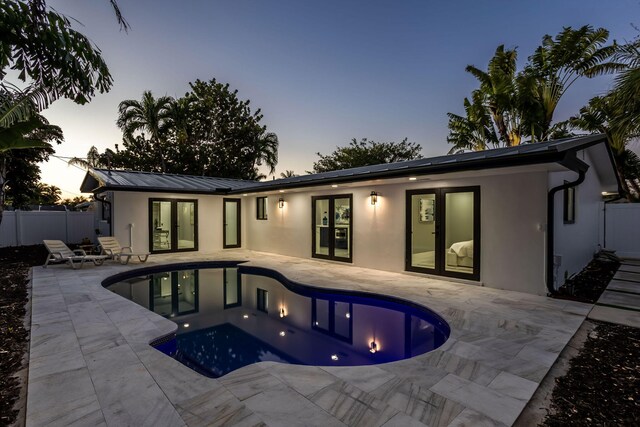 pool at dusk featuring french doors and a patio area