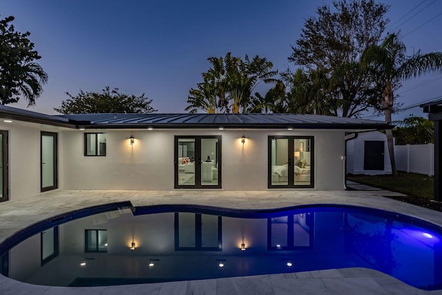 back house at dusk with a fenced in pool, a patio area, and solar panels