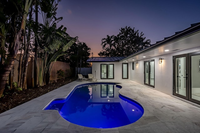 pool at dusk featuring a patio area and french doors