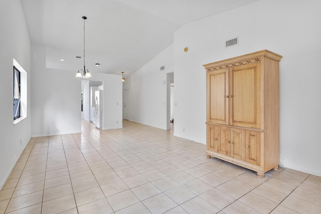 tiled spare room featuring a notable chandelier and high vaulted ceiling