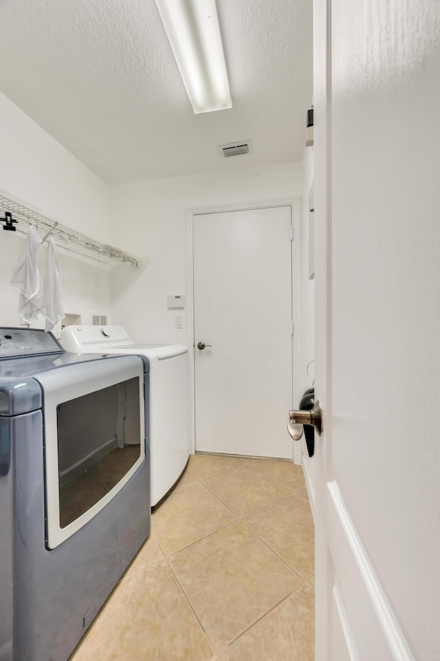 laundry room with independent washer and dryer, a textured ceiling, and light tile patterned flooring