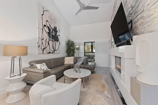 living room with hardwood / wood-style flooring, ceiling fan, a towering ceiling, and a fireplace