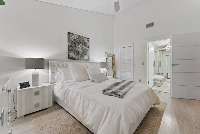 bedroom with light hardwood / wood-style flooring, ensuite bathroom, ceiling fan, and a high ceiling