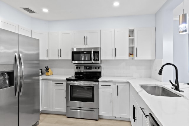 kitchen featuring appliances with stainless steel finishes, decorative light fixtures, tasteful backsplash, white cabinetry, and sink