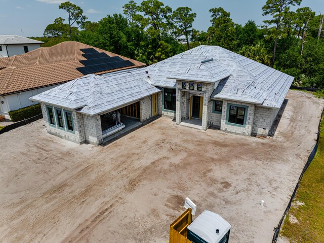 view of front of house featuring solar panels, stone siding, and dirt driveway