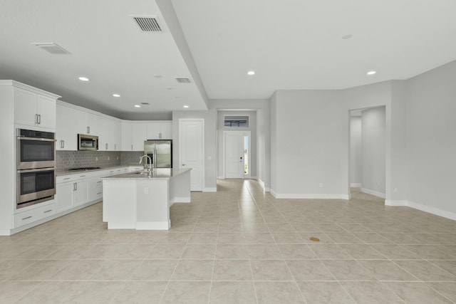 kitchen with appliances with stainless steel finishes, white cabinets, decorative backsplash, a kitchen island with sink, and light stone countertops