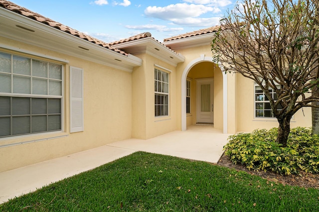 property entrance with a tiled roof, a patio area, and stucco siding