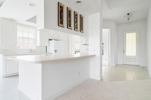 kitchen with light tile patterned floors, white cabinets, a peninsula, light countertops, and white fridge with ice dispenser