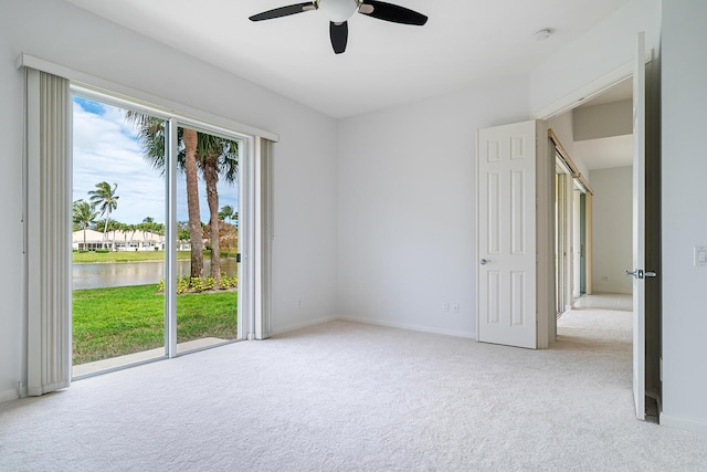 empty room featuring a ceiling fan, light colored carpet, a water view, and baseboards