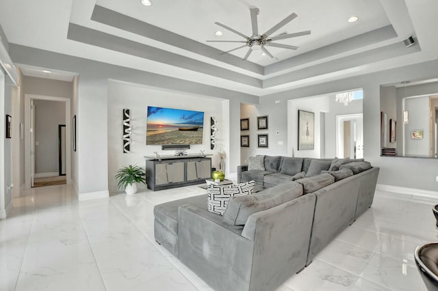 living room with a raised ceiling and ceiling fan with notable chandelier