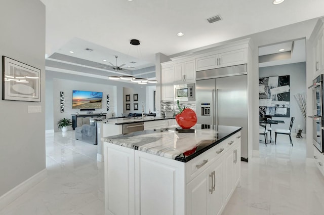 kitchen with a raised ceiling, white cabinetry, built in appliances, and kitchen peninsula