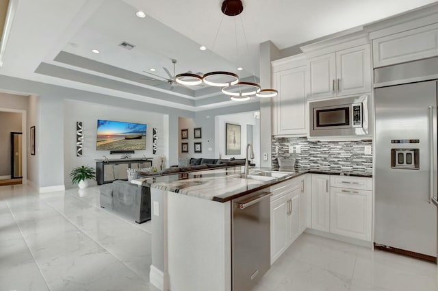 kitchen featuring white cabinetry, sink, dark stone counters, built in appliances, and a raised ceiling