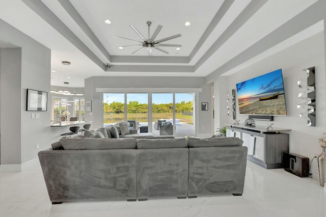 living room with a tray ceiling, a wealth of natural light, and ceiling fan