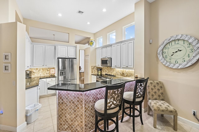 kitchen featuring visible vents, a peninsula, appliances with stainless steel finishes, a kitchen bar, and dark countertops