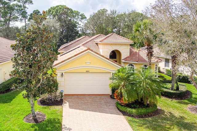 mediterranean / spanish-style home with a front lawn, a tile roof, stucco siding, decorative driveway, and a garage