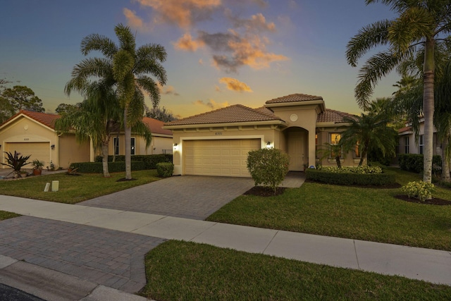 mediterranean / spanish-style home featuring a front lawn, decorative driveway, an attached garage, and stucco siding