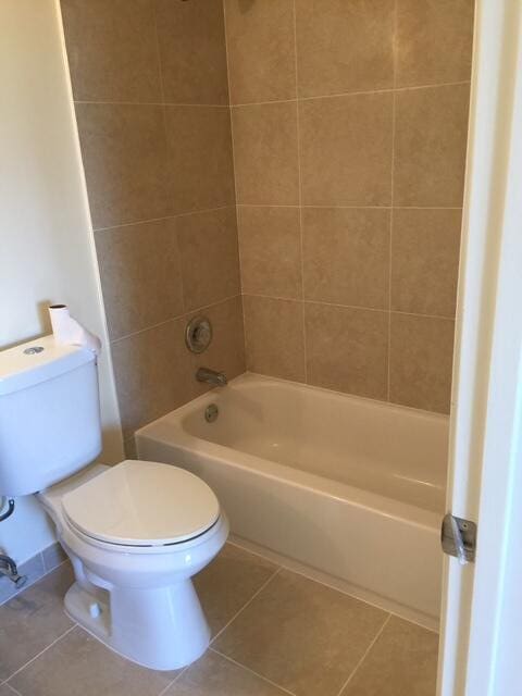 bathroom with tiled shower / bath combo, tile patterned floors, and toilet