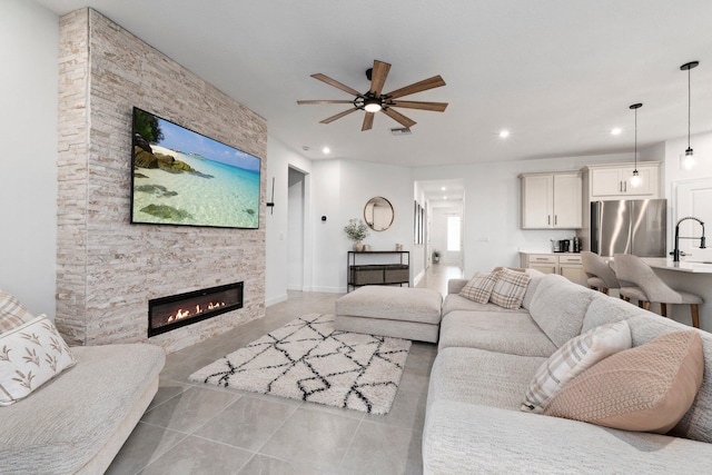 living room featuring ceiling fan, a stone fireplace, sink, and light tile patterned floors