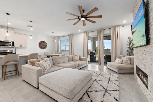 living room featuring ceiling fan, a fireplace, and light tile patterned floors