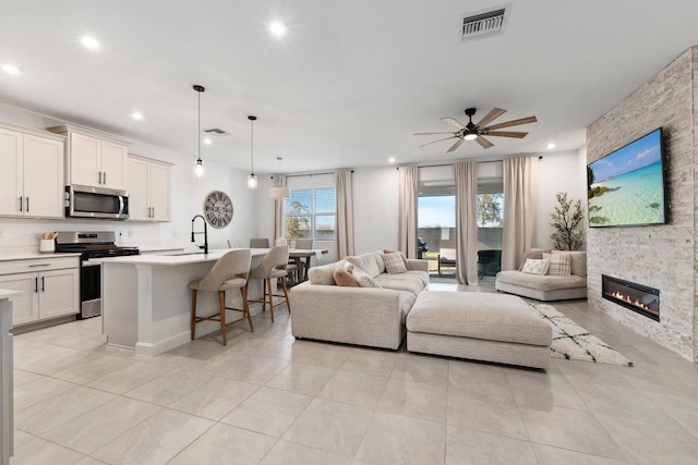 tiled living room featuring ceiling fan, sink, and a fireplace