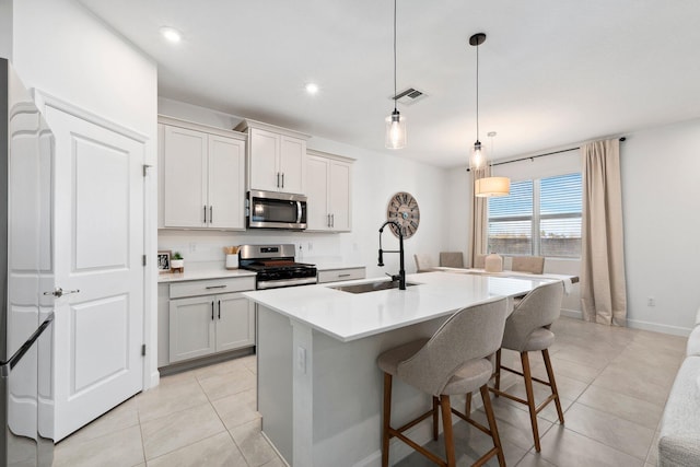 kitchen with a breakfast bar, sink, appliances with stainless steel finishes, an island with sink, and pendant lighting