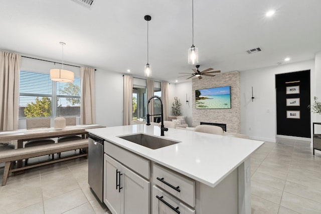 kitchen featuring sink, decorative light fixtures, stainless steel dishwasher, an island with sink, and a fireplace