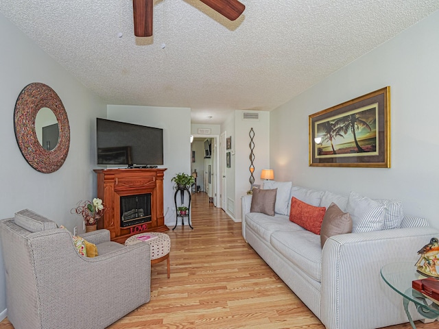 living room with ceiling fan, a textured ceiling, and light hardwood / wood-style flooring