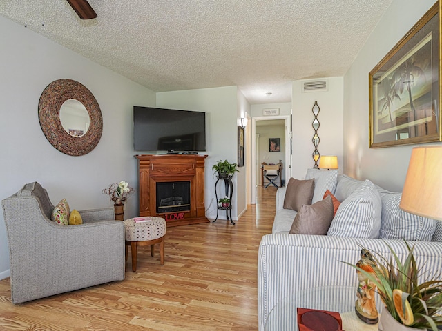 living room featuring ceiling fan, a textured ceiling, and light wood-type flooring