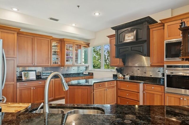 kitchen featuring sink, backsplash, stainless steel appliances, custom exhaust hood, and dark stone counters