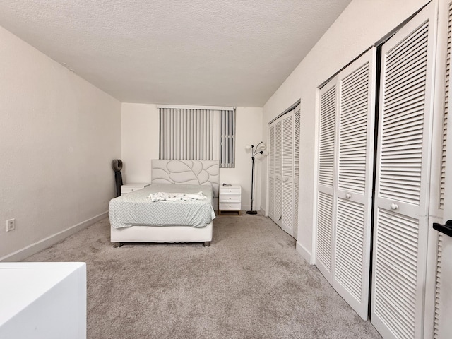 carpeted bedroom with baseboards, a textured ceiling, and multiple closets