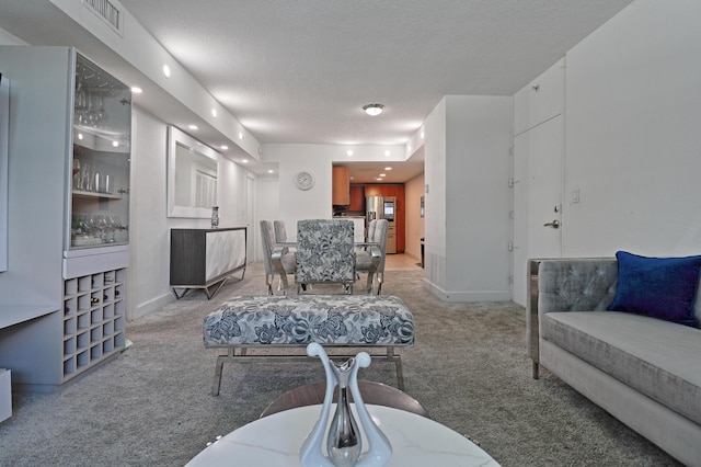 living area with baseboards, visible vents, a textured ceiling, and light colored carpet