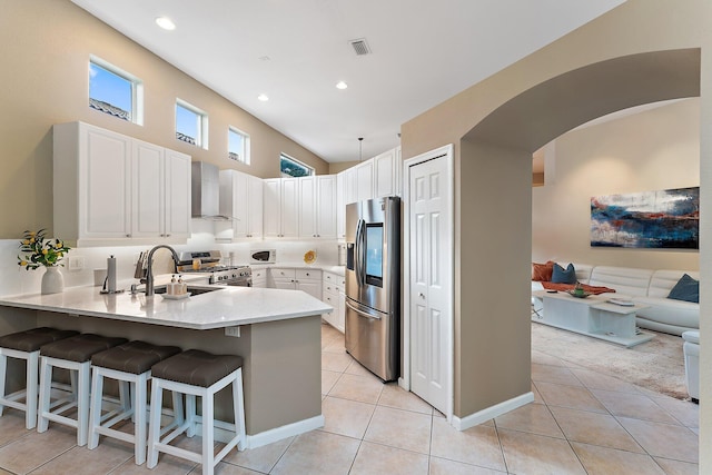 kitchen featuring stainless steel appliances, white cabinetry, a breakfast bar, and wall chimney exhaust hood