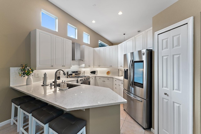 kitchen with stainless steel appliances, wall chimney range hood, a kitchen breakfast bar, and kitchen peninsula