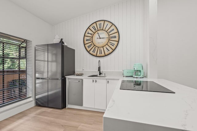 kitchen with sink, white cabinetry, light wood-type flooring, black electric cooktop, and stainless steel refrigerator