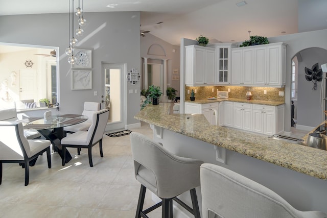 kitchen with ceiling fan, hanging light fixtures, light stone counters, white cabinets, and vaulted ceiling